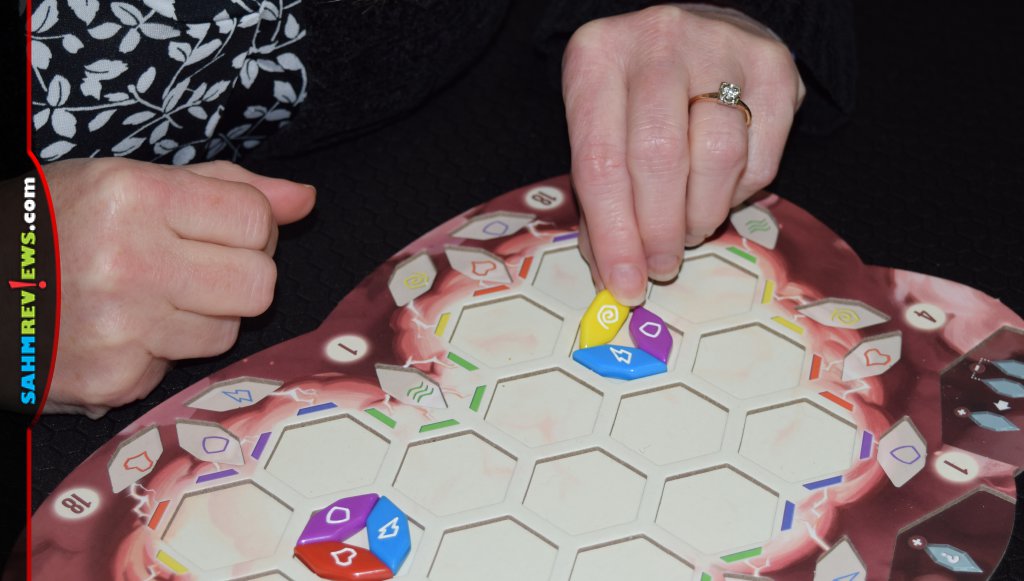 Hands of board gamer placing a fragment game piece into one of the hexagons on their board. - SahmReviews.com